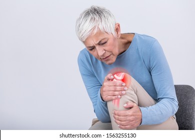 Senior Woman Holding The Knee With Pain. Old Age, Health Problem And People Concept - Senior Woman Suffering From Pain In Leg At Home. Elderly Woman Suffering From Pain In Knee At Home