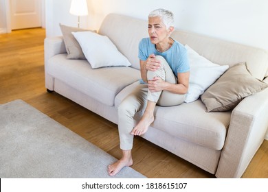 Senior Woman Holding The Knee With Pain. Old Age, Health Problem And People Concept - Senior Woman Suffering From Pain In Leg At Home. Elderly Woman Suffering From Pain In Knee At Home