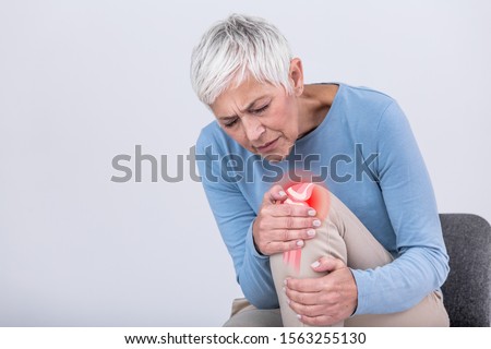 Senior woman holding the knee with pain. Old age, health problem and people concept - senior woman suffering from pain in leg at home. Elderly woman suffering from pain in knee at home
