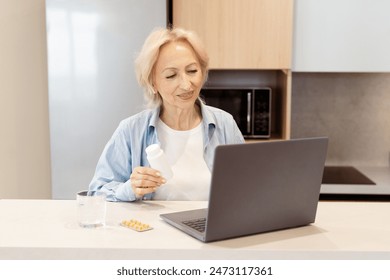 Senior Woman Holding Medication While Using Laptop In Kitchen, Elderly Care And Online Health Consultation Concept - Powered by Shutterstock