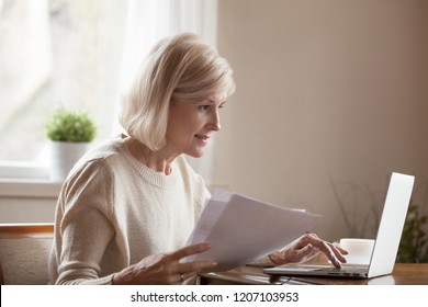 Senior woman holding papers busy at laptop managing house utility bills or finances, aged female using computer working with bank loan or mortgage documents online. Elderly and technology concept - Powered by Shutterstock