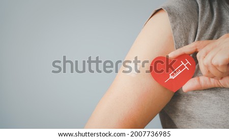 senior woman holding red heart shape with  syringe and showing her arm with bandage after got vaccinated or inoculation due to spread of corona virus, population, social or herd immunity concept

