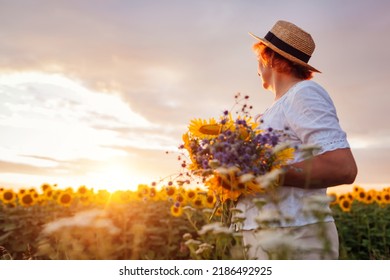 Senior woman holds bouquet of yellow sunflowers in summer field at sunset. Middle-aged woman admires landscape - Powered by Shutterstock