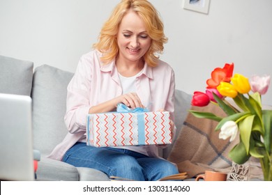 Senior Woman At Home Celebration Sitting On Sofa Opening Present Box Smiling Excited