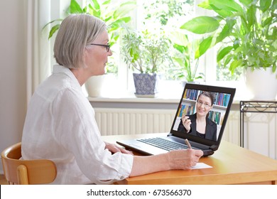 Hohe Frau zu Hause vor ihrem Laptop, die beim Betrachten eines Online-Videos von Steuerberatung durch eine Buchhalterin Notizen macht