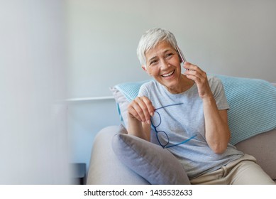 Senior Woman At Home On The Couch Talking On Cell Phone. Cheerful Woman Making A Phone Call Lying On Bed. Technology, Communication And People Concept, Happy Senior Woman Calling On Smartphone At Home