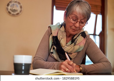 Senior Woman At Home Sitting At Table And Writing In Notebook Or Journal