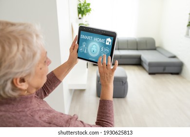 Senior woman at home standing at kitchen holding digital tablet controlling smart home system back view checking cameras close-up - Powered by Shutterstock