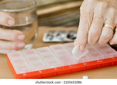 Senior Woman At Home Taking Pills From A Box To Take With A Glass Of Water. Headaches, Depression, Medication Supplements, Vitamins, Sedatives. Pillbox To Organize Weekly Shots