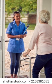 Senior Woman At Home Using Walking Stick Greeting Female Nurse Or Care Worker In Uniform At Door