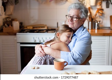 Senior woman hugging child at home. Happy family enjoying kindness, support, care together in cozy kitchen. Cute girl visiting grandmother. Lifestyle moments. Holiday Thanksgiving.