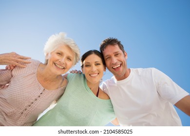Senior woman hugging couple against blue sky