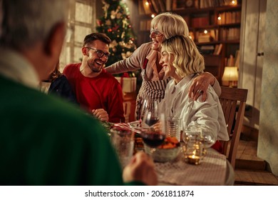 Senior Woman Hugging Her Daughter And Son In Law While Sitting At The Table During Christmas Time