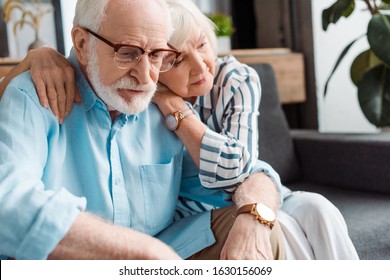 Senior woman hugging sad husband on couch at home - Powered by Shutterstock