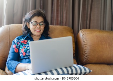 Senior Woman Or Indian Senior Woman Wearing Glasses Lying On A Sofa At Home Concentrating As She Works On A Laptop And Shopping Online Concept.Social Distancing Work From Home.Online Class Education.