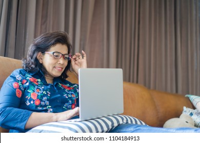 Senior Woman Or Indian Senior Woman Wearing Glasses Lying On A Sofa At Home Concentrating As She Works On A Laptop And Shopping Online Concept.Social Distancing Work From Home.Online Class Education.