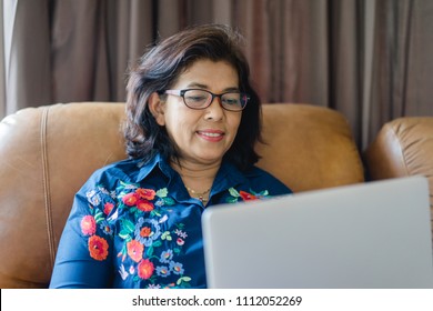 Senior Woman Or Indian Senior Woman Wearing Glasses Lying On A Sofa At Home Concentrating As She Works On A Laptop And Shopping Online Concept.Social Distancing Work From Home.Online Class Education.