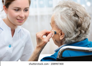 Senior Woman Inserts Hearing Aid In Her Ear