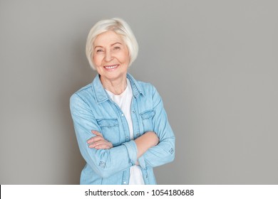 Senior Woman In Jeans Jacket Studio Isolated On Grey Wall Crossed Arms Happy