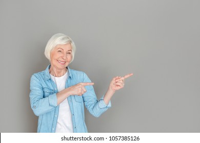 Senior Woman In Jeans Jacket Studio Isolated On Grey Wall Pointing Aside Copyspace