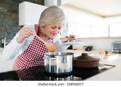 Senior woman in the kitchen cooking, mixing food in a pot.