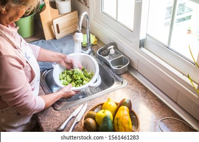 A senior woman in the kitchen washing the broccoli. Some tropical fruit close to her. Healthy eating - Powered by Shutterstock