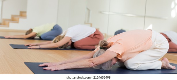 Senior Woman Kneeling In Child's Pose During Group Yoga Training.