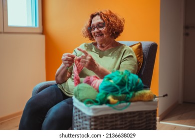 Senior Woman Knitting Crochet Slipper While Relaxing At Home In Her Armchair. Elderly Leisure Activities For Good Mental Health Concept. Art And Craft Concept.