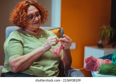 Senior Woman Knitting Crochet Slipper While Relaxing At Home In Her Armchair. Elderly Leisure Activities For Good Mental Health Concept. Art And Craft Concept.