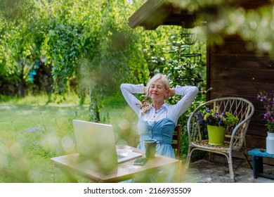 Senior woman with laptop and coffee sitting on terrace in summer, resting. - Powered by Shutterstock