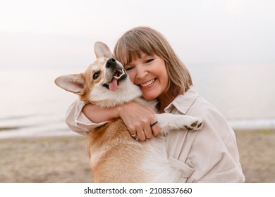 Senior woman laughing and playing with her dog while resting on sandy beach