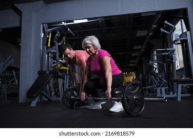 Senior Woman Learning Barbell Deadlift Exercise With Personal Trainer At The Gym