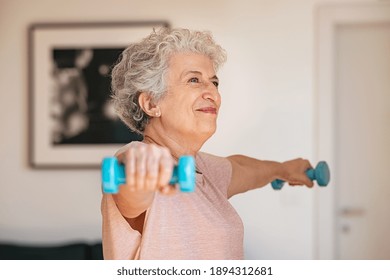 Senior Woman Lifting Weights And Working Out At Home. Old Woman Doing Arms Stretching Exercise Using Weight Dumbbells. Retired Lady Exercising With Light Weights.