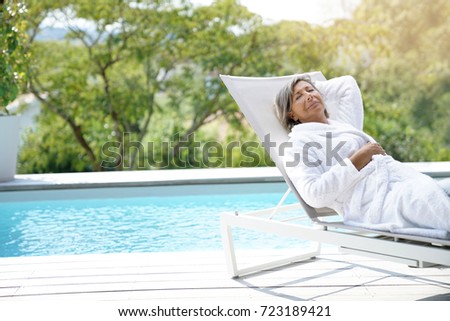 Senior woman in long chair relaxing by the pool
