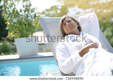 Senior woman in long chair relaxing by the pool