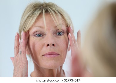 Senior Woman Looking At Her Skin In Mirror