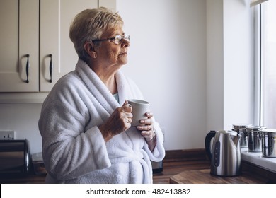 Senior woman looking out of her kitchen window with a cup of tea in hand.  - Powered by Shutterstock