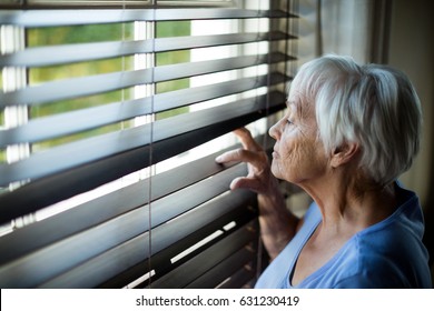 Senior woman looking out from window blind at home - Powered by Shutterstock