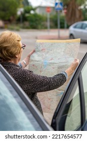 Senior Woman Looking At A Paper Map Leaning Against A Car