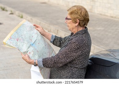 Senior Woman Looking At A Paper Map Leaning Against A Car