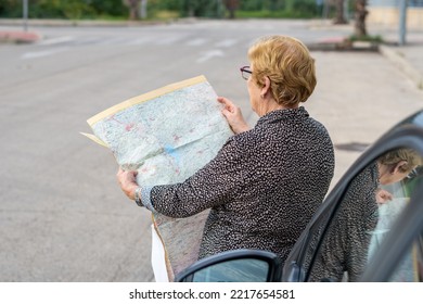 Senior Woman Looking At A Paper Map Leaning Against A Car