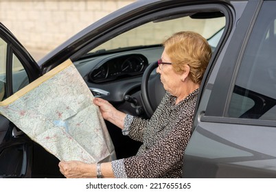 Senior Woman Looking At A Paper Map Sitting In A Car. 


