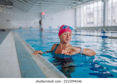 Senior woman looking at smartwatch when swimming in indoors swimming pool.