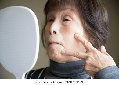 Senior woman looks in the mirror and is worried about the aging phenomenon - Powered by Shutterstock