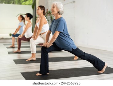 Senior woman maintaining mental and physical health attending group yoga class at health sports studio, practicing stretching poses - Powered by Shutterstock