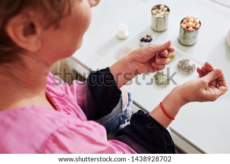Senior woman making bracelets at home, focus of string with transparent beads