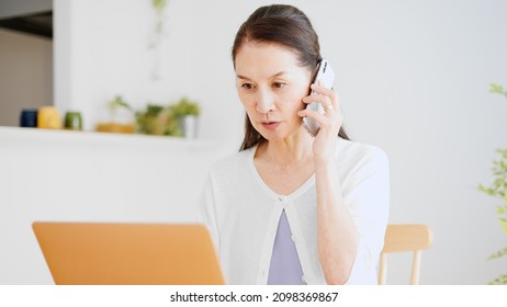 A Senior Woman Making A Phone Call While Looking At Her Computer.	