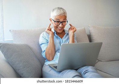 Senior Woman Making Video Call On Laptop , Waving At Screen, Chatting Online With People Who Distance. Cropped Shot Of A Happy Senior Woman Waving Hello While On A Video Call On Her Couch At Home