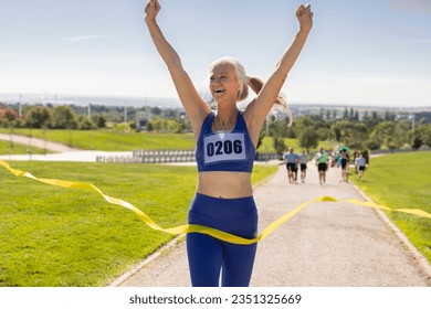 senior woman marathon runner, with bib number, wins the race and celebrates it at the finish line - Powered by Shutterstock