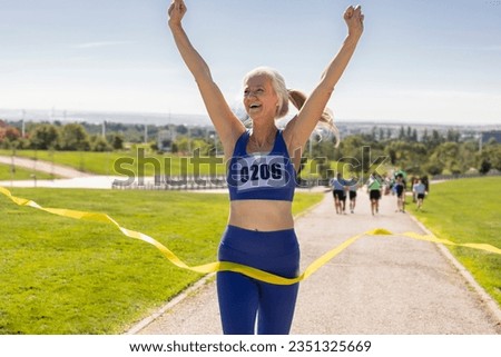 senior woman marathon runner, with bib number, wins the race and celebrates it at the finish line